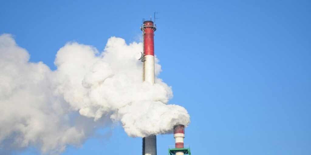 Red industrial smoke stacks against a clear blue sky, symbolizing manufacturing compliance and VOC emissions control.